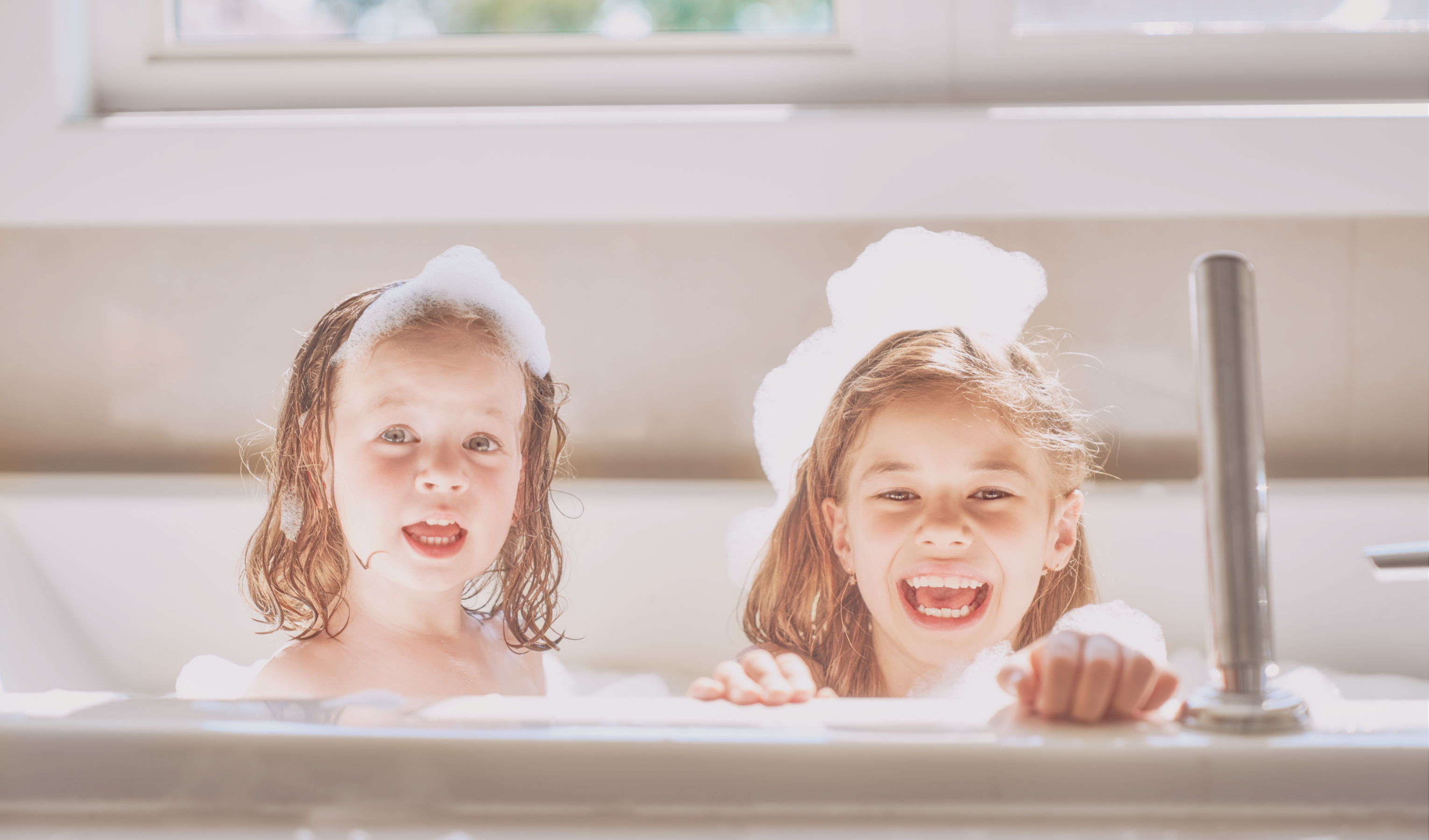 two children in bath tub with bath foam on head