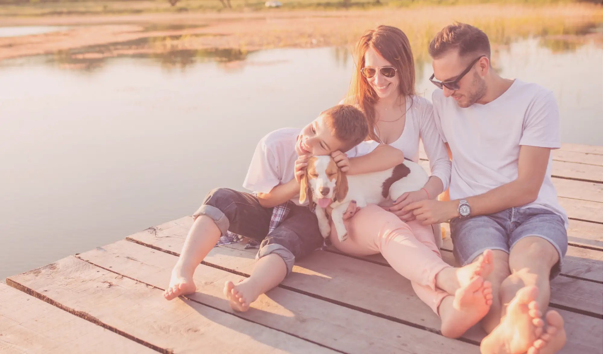 family with one child and dog sitting on a pier 