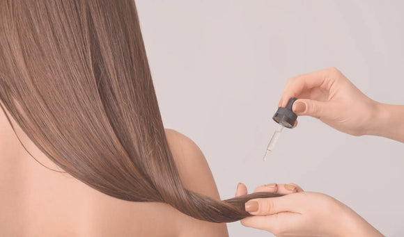 Lady with long brown hair with someone applying an oil treatment to the ends of her hair