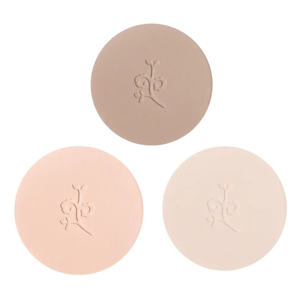 Three circular pressed powder compacts in different nude and beige tones with embossed floral designs.