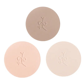 Three circular pressed powder compacts in different nude and beige tones with embossed floral designs.