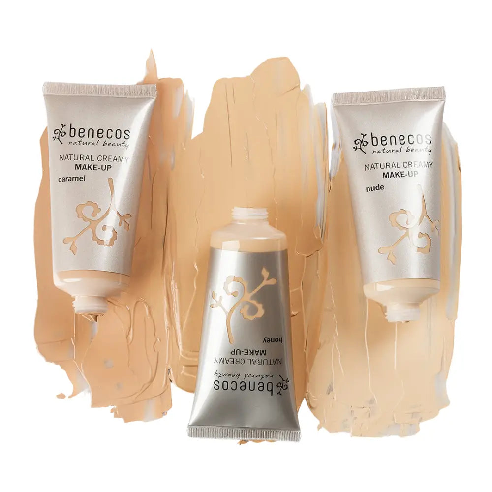 Three tubes of Benecos natural cream makeup with beige-toned swatches behind them.