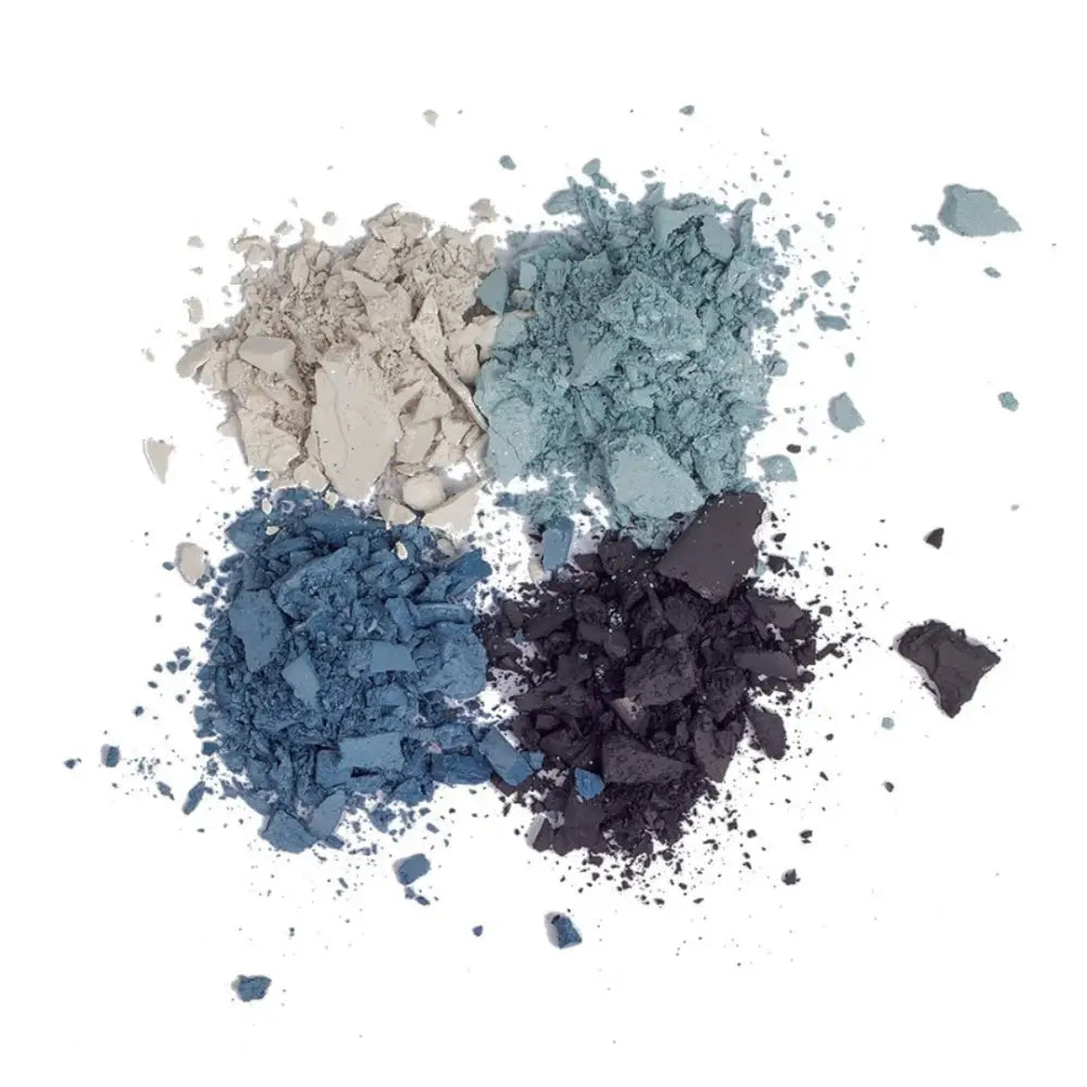 Crushed eyeshadow powders in shades of blue, gray, and black scattered on a surface.