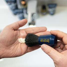 Blue-handled shaving brush with lather.