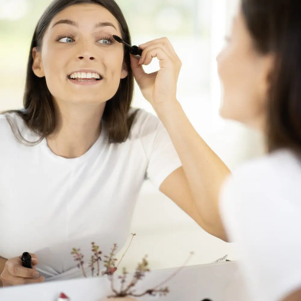 Someone applying mascara while smiling in a mirror.