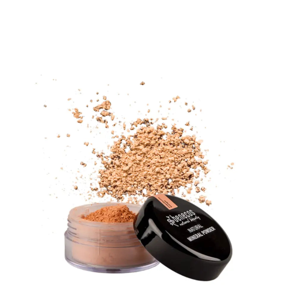 Open jar of loose mineral makeup powder in a peachy-beige shade with scattered powder above it.