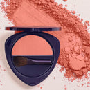 Navy blue compact powder case with coral-colored blush and a makeup brush.