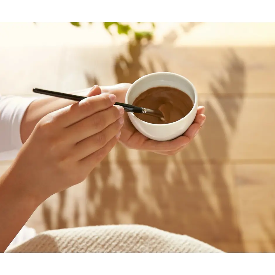 Hands holding a white ceramic cup filled with coffee or hot chocolate.