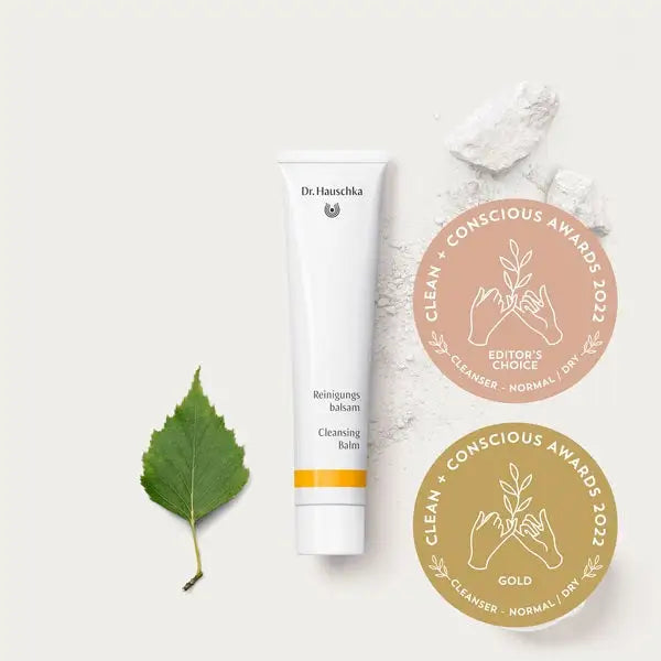 White tube of Dr. Hauschka cleansing balm with a green leaf and two circular award medals beside it.