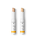 Two white Dr. Hauschka cover stick concealers with beige tips.