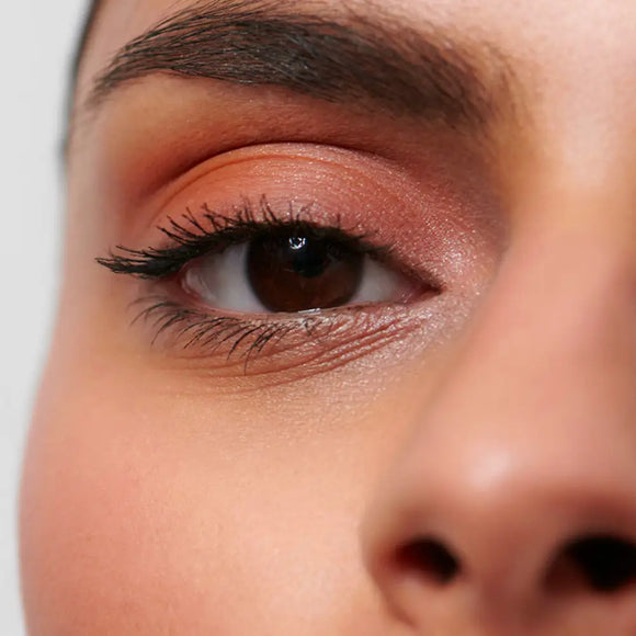 Close-up of a brown eye with peachy-coral eyeshadow and mascara.