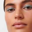 Close-up shot of brown eyes with shimmery mint green eyeshadow and glossy nude lips.