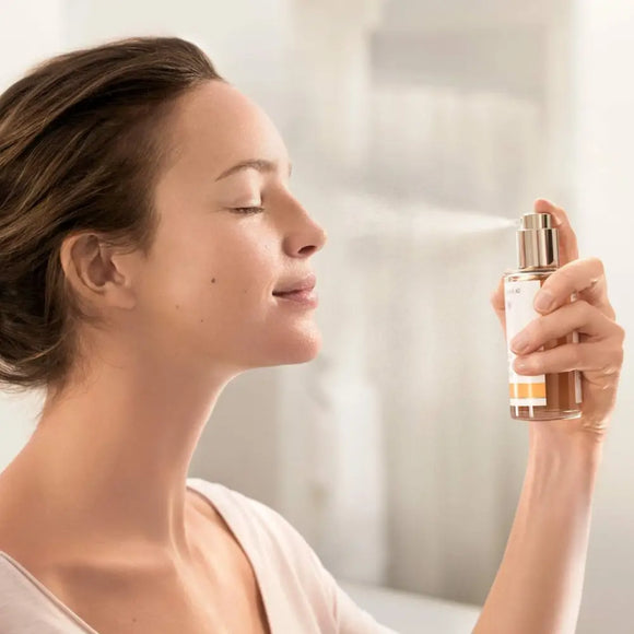 A glass perfume bottle being sprayed with closed eyes.