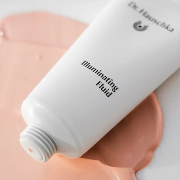 White cosmetic tube containing illuminating fluid with product dispensed in a peachy tone.