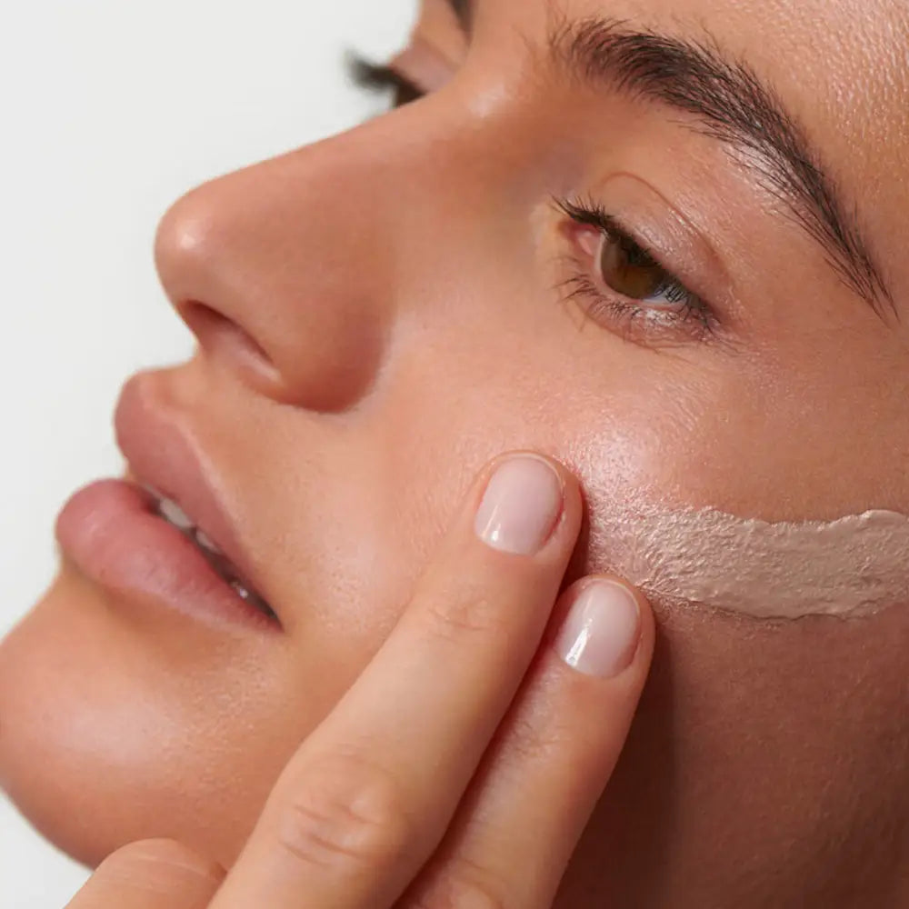 A finger applying moisturizer or skincare product to the cheek.