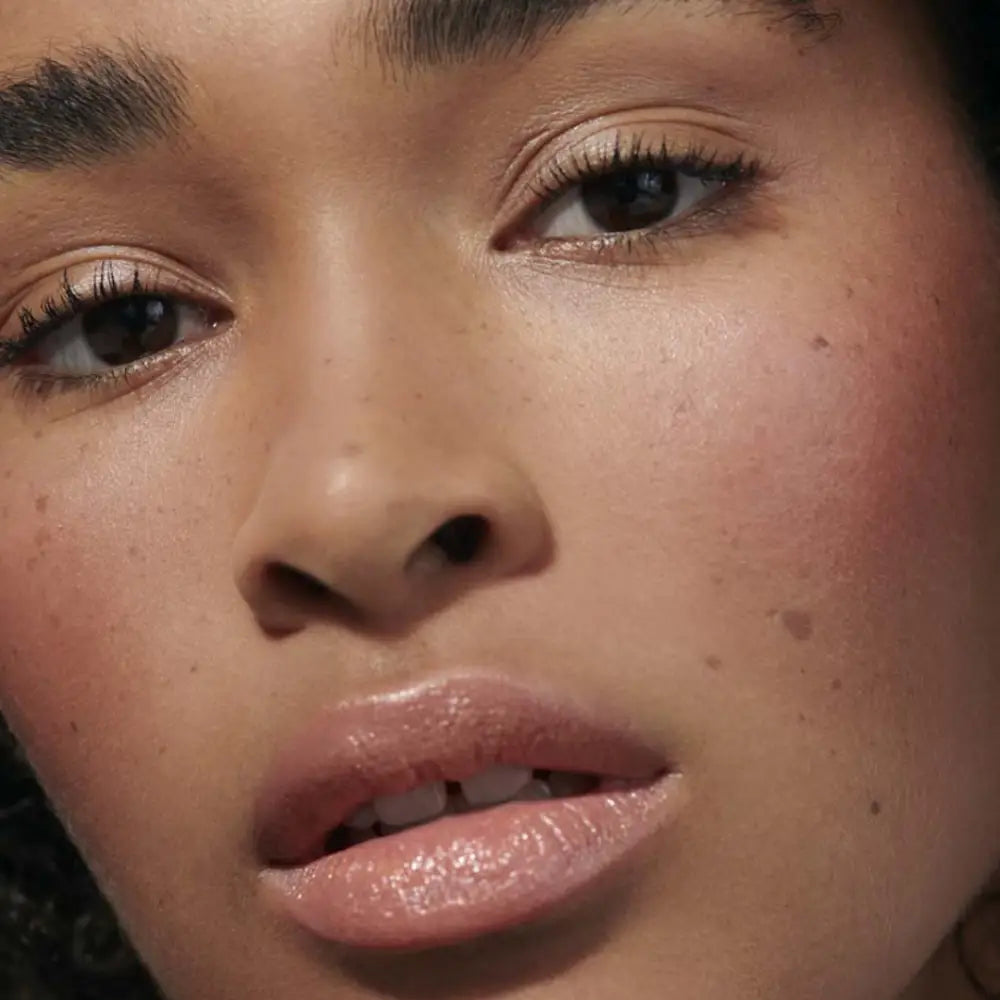 Close-up portrait showing glossy lips, warm brown eyes, and glowing skin.