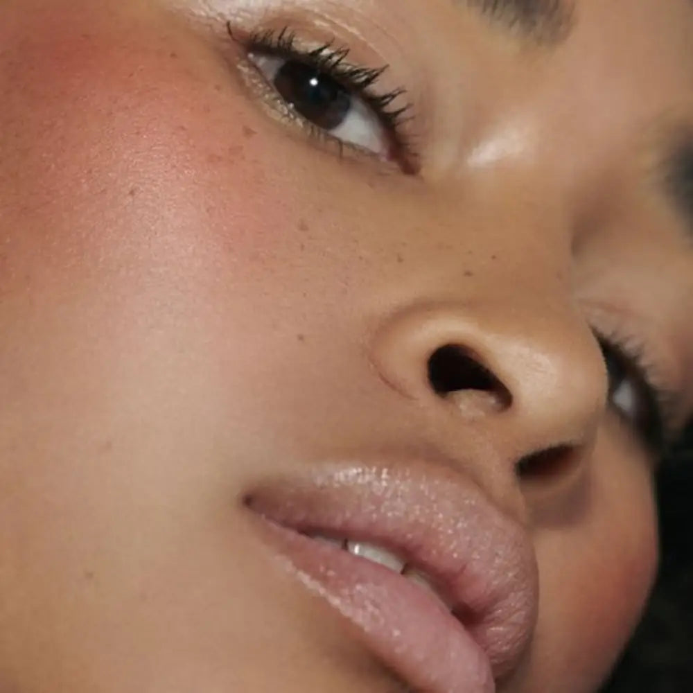 Close-up beauty shot showing glossy lips, dark lashes, and glowing skin.