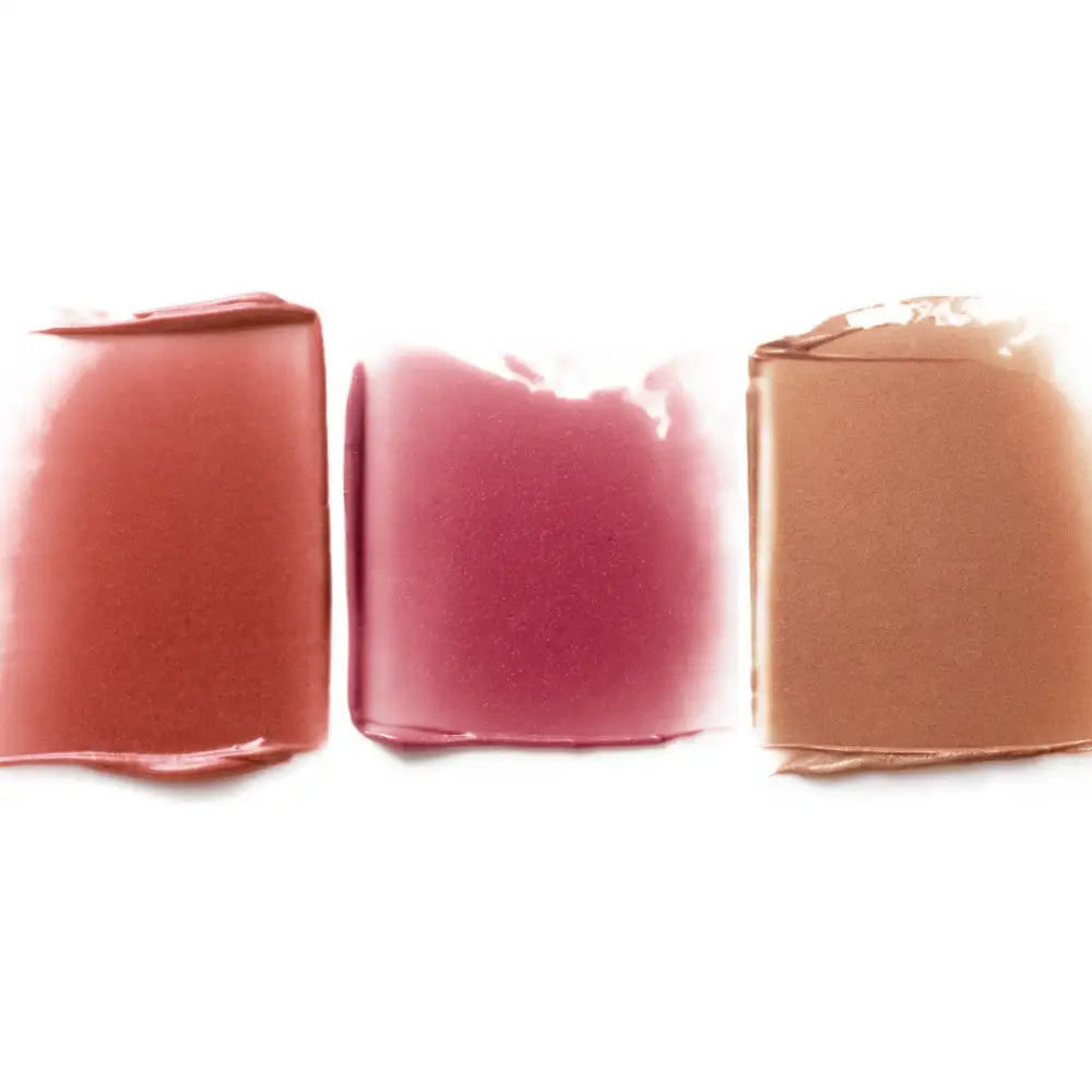 Three smeared swatches of makeup in coral, pink, and nude shades.