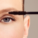 A woman’s eye with a mascara wand applying product to her eyelashes.