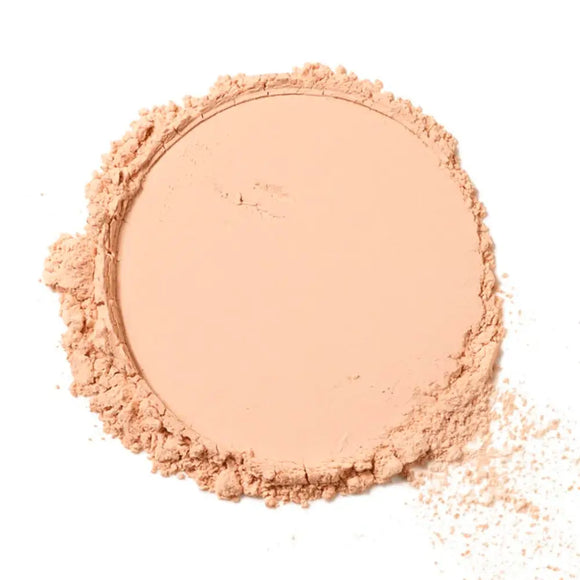 Pressed powder makeup compact in a light peachy-beige shade with scattered loose powder around the edges.