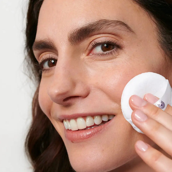 Cotton pad being used to apply skincare product to the face.