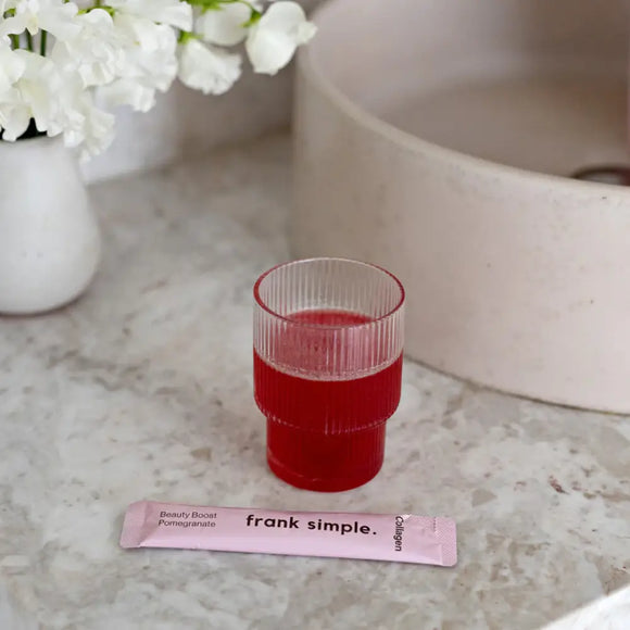 Glass of red liquid next to a pink packet labeled ’frank simple.’