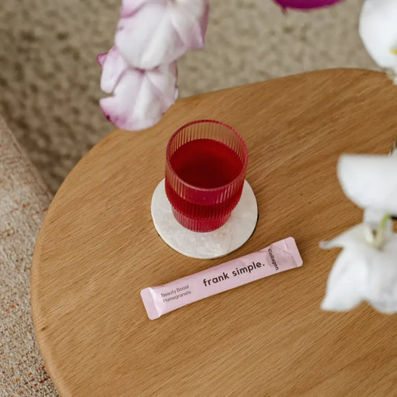 Red beverage in a ribbed glass with a ’frank simple’ packet on a coaster.