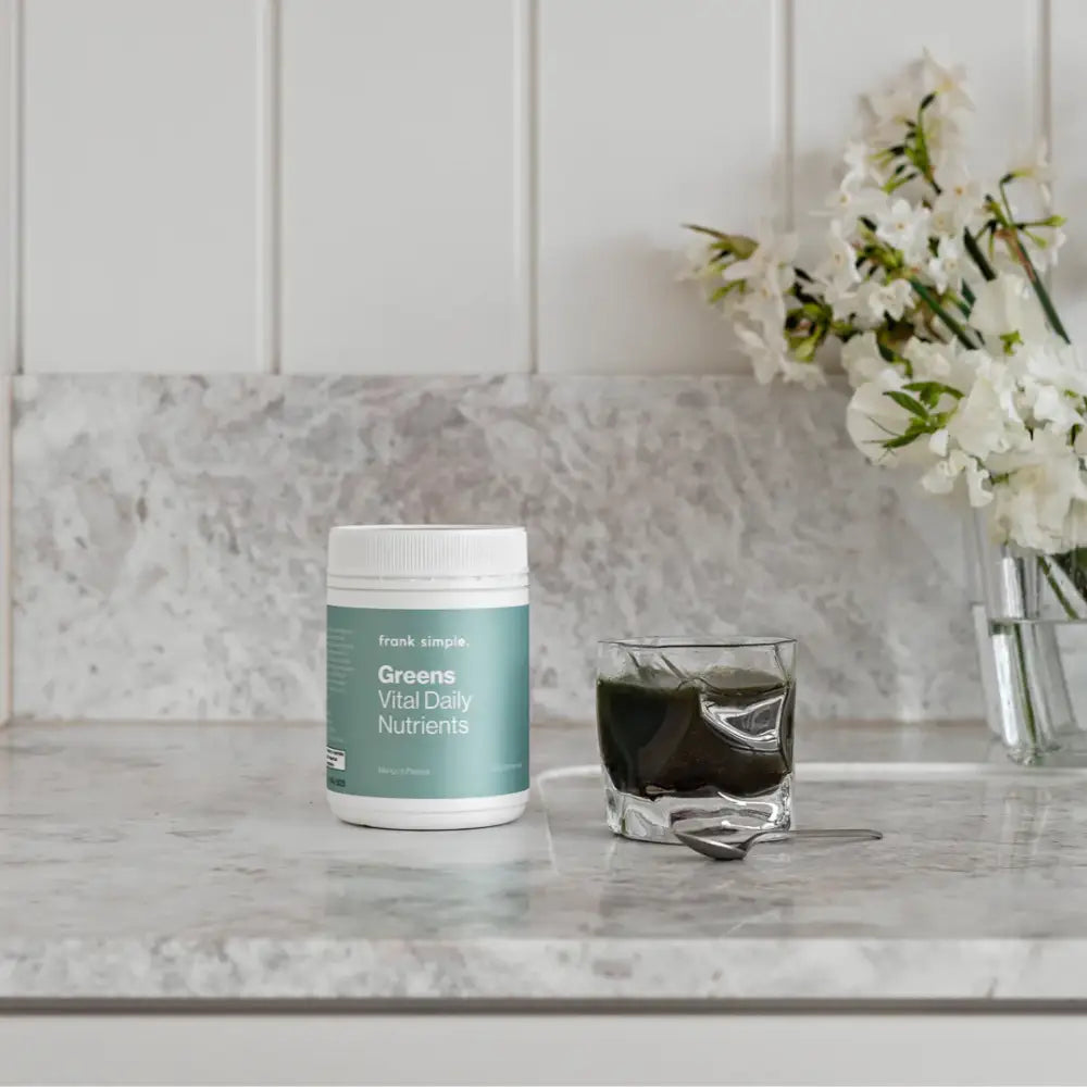 A green and white supplement container sits next to a glass of dark liquid.