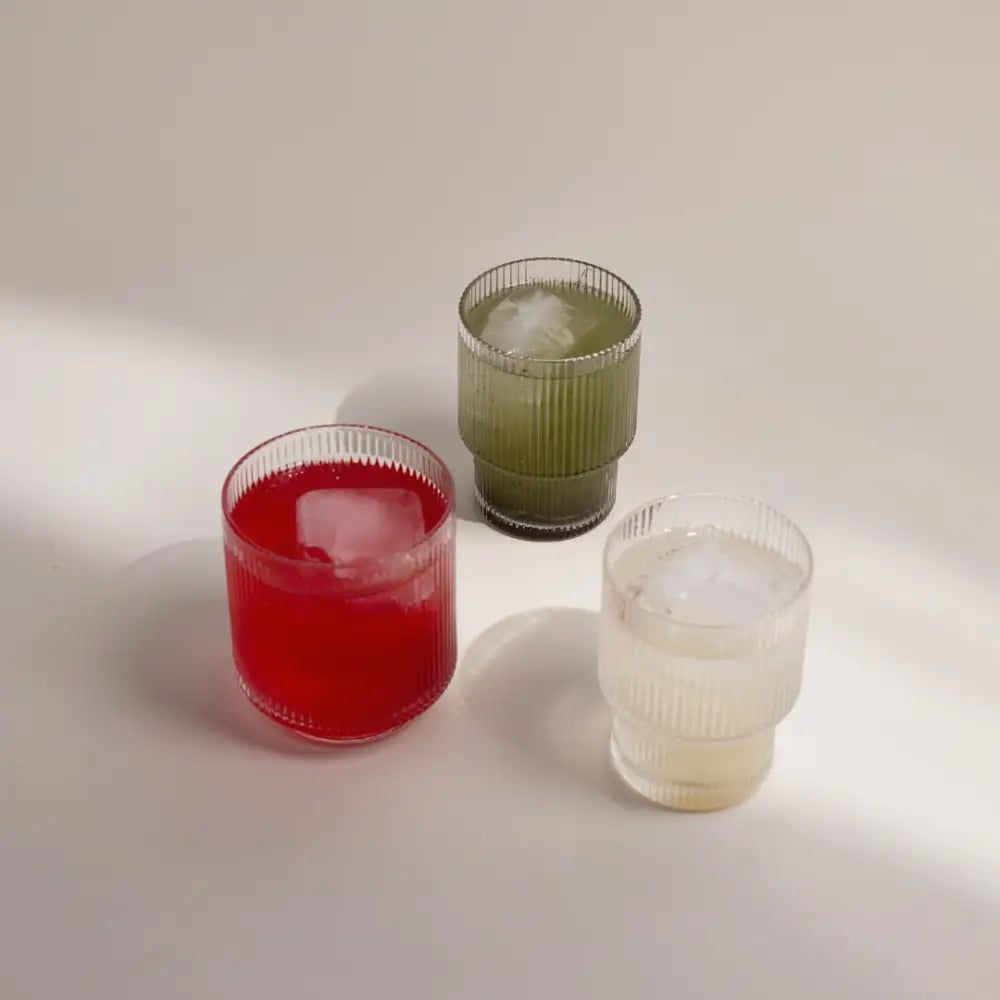 Three ribbed glass tumblers containing red, green, and clear beverages.