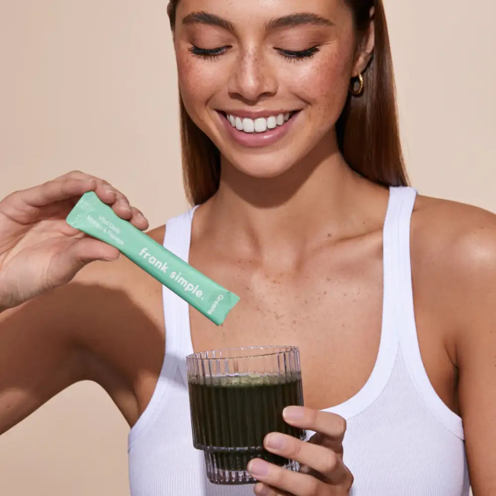 A green powder supplement being poured into a glass of dark liquid.