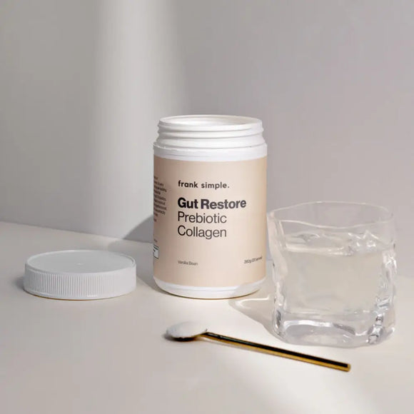 A jar of Frank Simple Gut Restore Prebiotic Collagen supplement with its lid and a gold spoon.