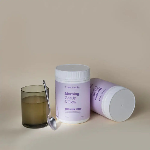 Purple and white supplement container labeled ’Morning Get Up & Glow’ with a glass of liquid and spoon beside it.