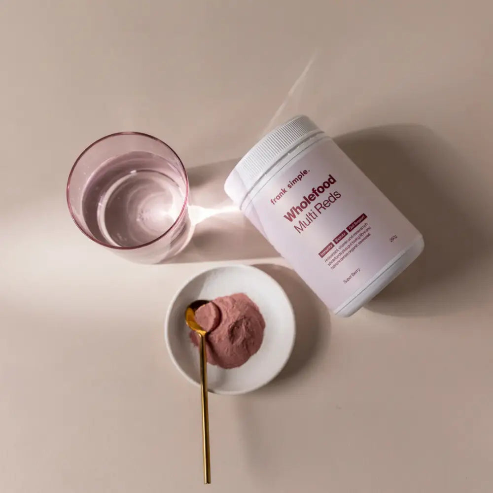 White supplement container with pink powder on a small plate beside a glass of water.