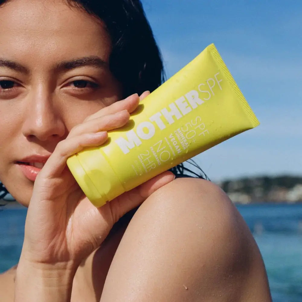 Yellow sunscreen tube being held up against blue water.