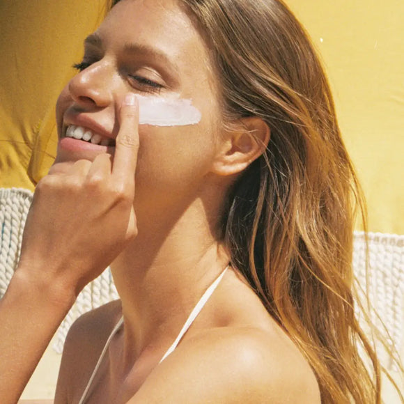 woman applying mother spf 50 sunscreen to her cheek in sunlight.