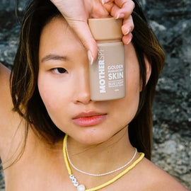 A bottle of ’Golden Skin’ beauty product held against dark hair.