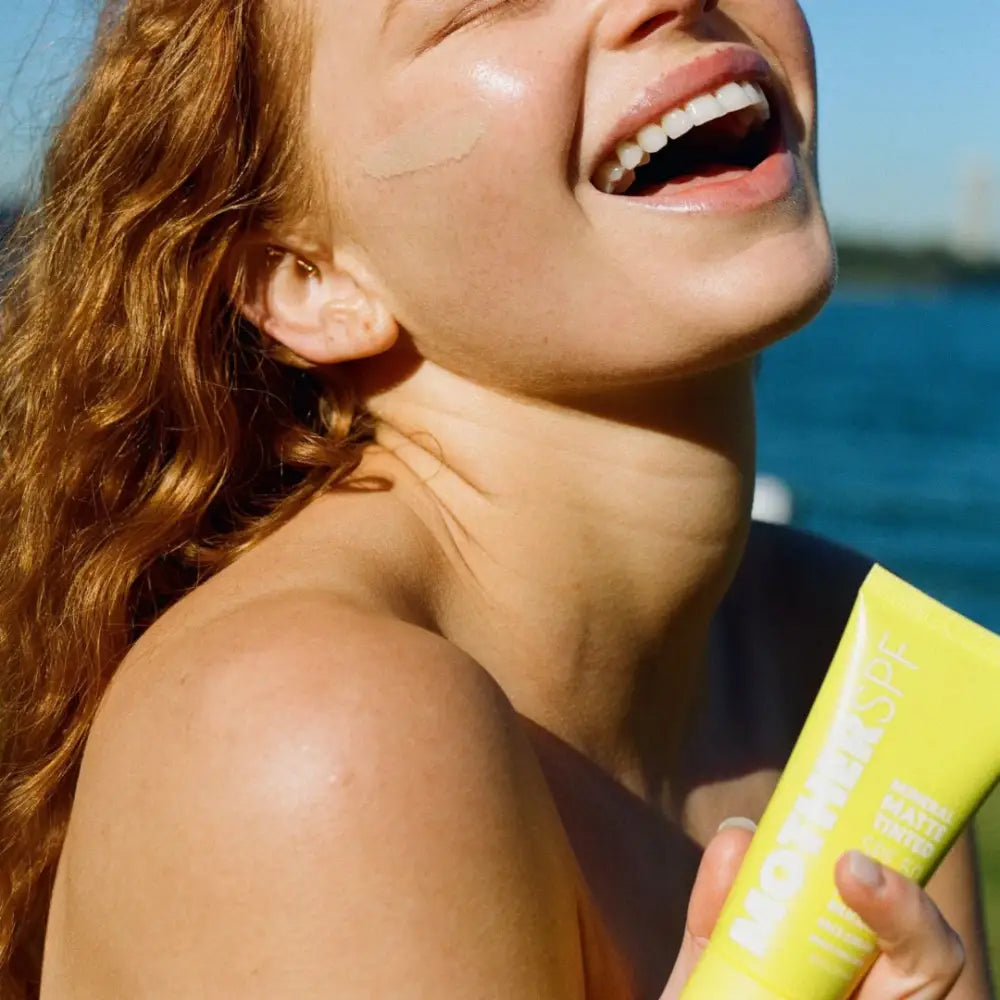 A bright yellow tube of sunscreen being held in sunlight.