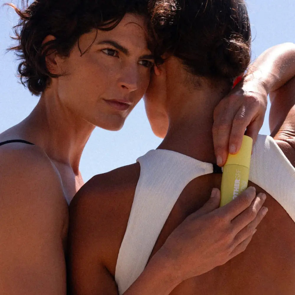 A yellow sunscreen bottle being held between two people in an intimate pose.