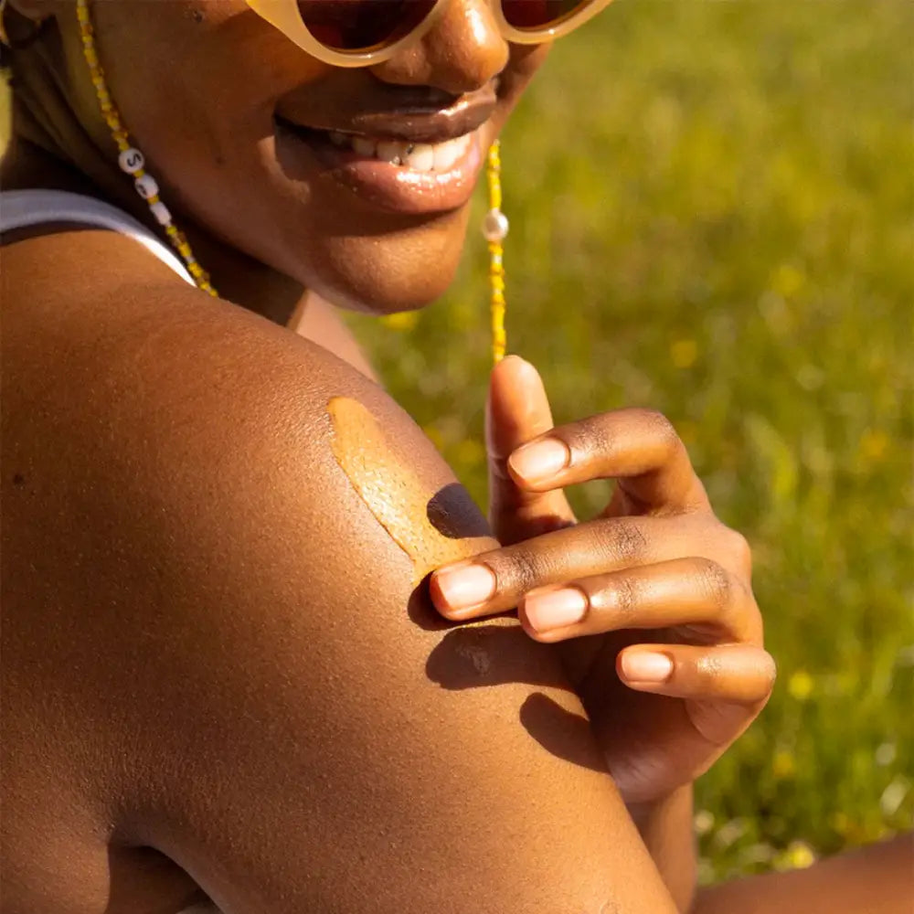 A smiling person wearing sunglasses and white nail polish in sunlit conditions.