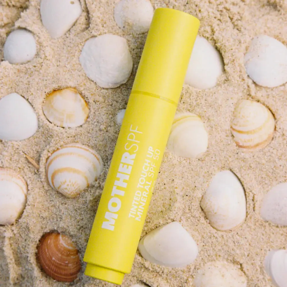 Yellow lip balm or sunscreen stick against seashells and sand.