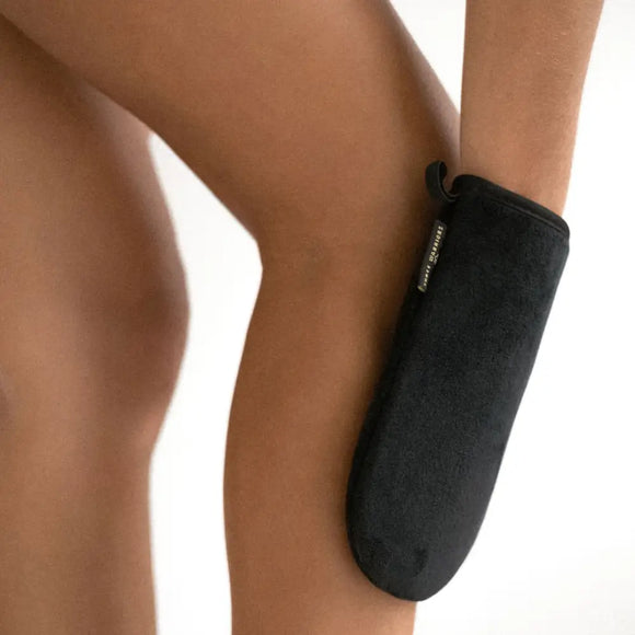 Black tanning mitt being used on a leg.