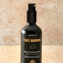 Black spray bottle labeled ’Three Warriors Face Tan Aqua Mist’ with a minimalist mountain logo.