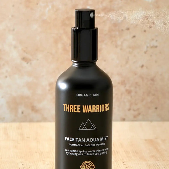 Black spray bottle labeled ’Three Warriors Face Tan Aqua Mist’ with a minimalist mountain logo.