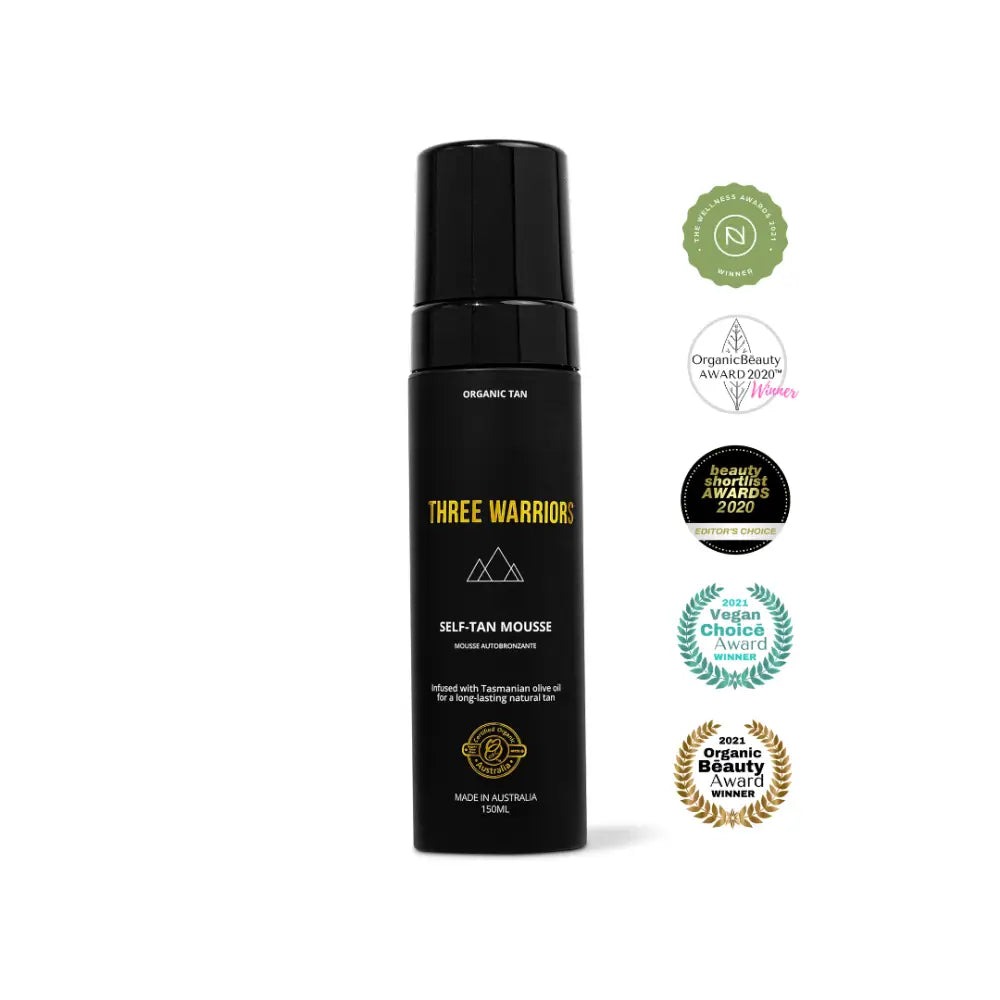 Black bottle of Three Warriors self-tanning mousse with award badges displayed alongside it.