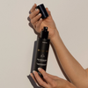 Three warriors body tan aqua mist being held by a woman's hands. Lid off in hands showing the spray-nozzle